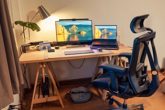 Innenarbeitsplatz mit Laptop-Monitor, Computergerät, Beleuchtungslampen, grünem Blatt auf Holztisch und ergonomischem Stuhl