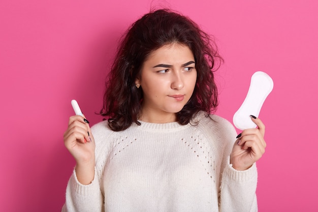 Innenaufnahme der jungen brünetten Frau, die zwei intime Produkte hält