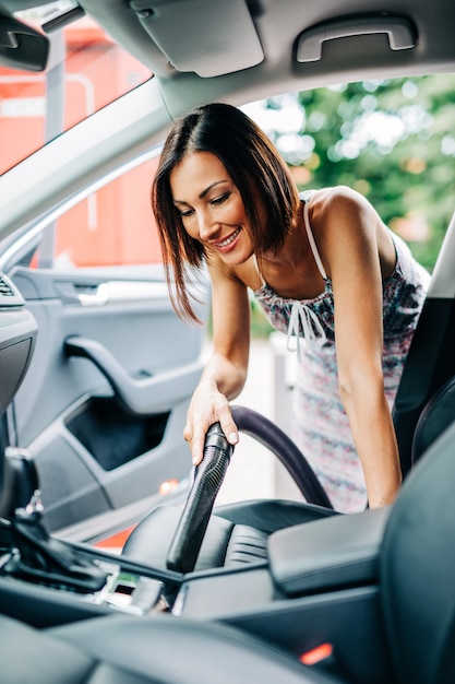 Innenausstattung des Autos. Glückliche Frau mittleren Alters reinigt den Innenraum ihres Autos mit Staubsauger.