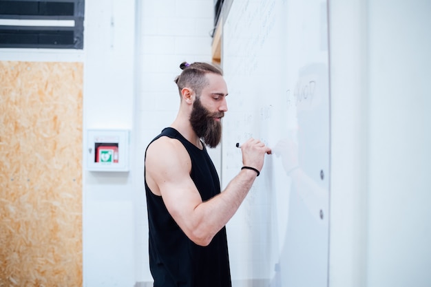 Innengymnastikschreiben des persönlichen Trainers des jungen Mannes auf whiteboard Planungstraining