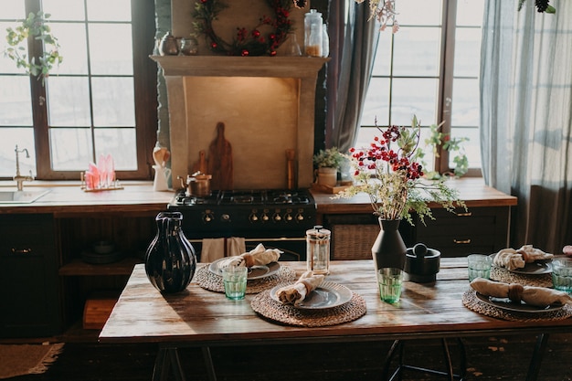 Innenraum der Küche. Serviert Esstisch mit Teller Gläser Blumendekor. Besteck und Glaswaren. Vorbereitung für das festliche Abendessen. Tischdekoration für das Familienessen