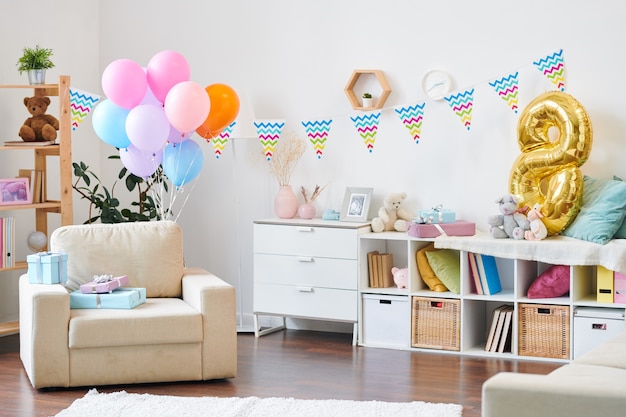 Innenraum des Wohnzimmers in der modernen Wohnung für Geburtstagsfeier der kleinen Kinder vorbereitet und mit Luftballons und Fahnen verziert