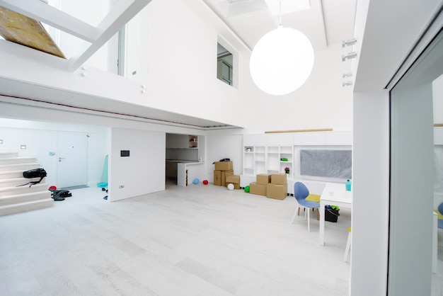 Innenraum einer leeren, stilvollen, modernen, offenen Wohnung auf zwei Ebenen mit weißen Wänden und einem großen runden Kronleuchter in der Mitte, bereit zum Einzug