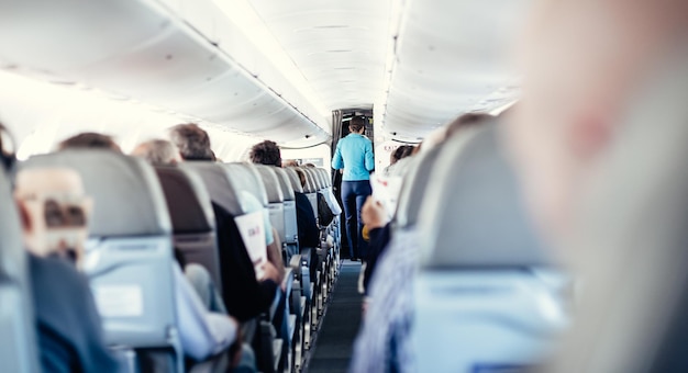 Innenraum eines Flugzeugs mit Passagieren auf Sitzen und einer Stewardess in Uniform, die durch den Gang geht und Personen bedient