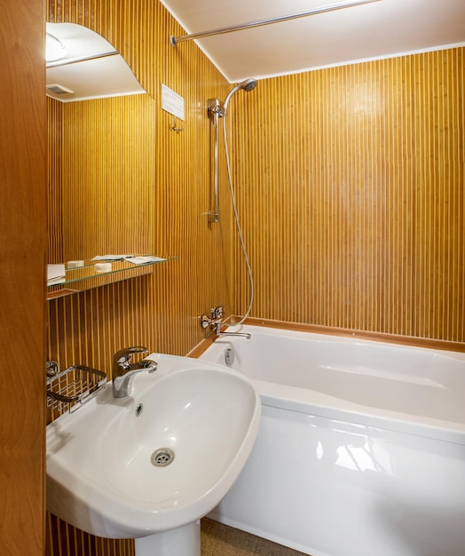 Innenraum eines kleinen Badezimmers im Hotelzimmer mit Holzwänden, weißem Waschbecken und Badewanne