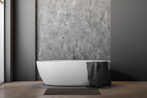 Innenraum eines minimalistischen Badezimmers mit grauen Betonwänden, Betonboden, großem Fenster und weißer Badewanne mit Handtuch darauf und grauem Teppich daneben. 3D-Rendering