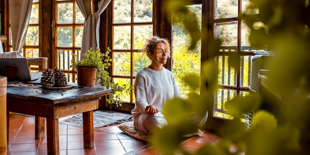 Foto innere ausgeglichenheit und liebe zu sich selbst konzept lebensstil eine junge frau mittleren alters meditiert in der yoga-asana-position zu hause auf dem boden sitzend gesunde natürliche bewegung geistiges wohlbefinden