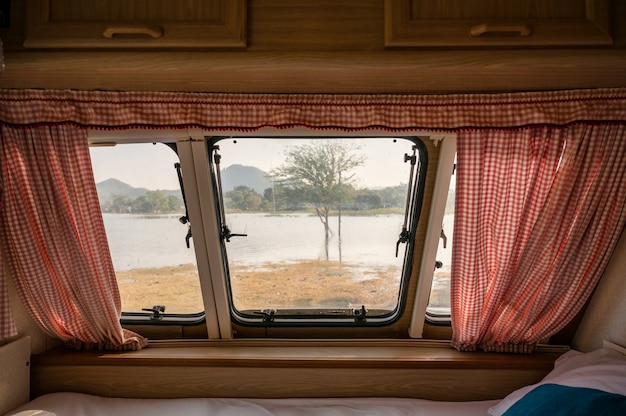 Inneres leeres Bett im Wohnmobil und der Blick durch das Fenster mit Vorhang auf den See