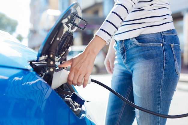 Innovaciones en la industria del automóvil. Agradable y agradable joven sosteniendo un cargador de automóvil y usándolo para su automóvil mientras visita un lugar de carga