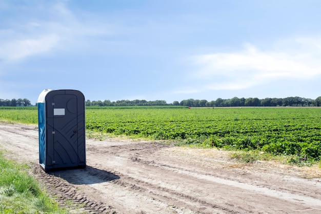 Inodoro portátil de plástico público en el campo agrícola del paisaje del agricultor con el cielo azul al aire libre