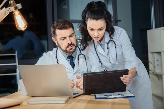 Inovações modernas. Cientistas profissionais sérios e inteligentes olhando para a tela do tablet e aprendendo sobre inovações modernas enquanto trabalham juntos