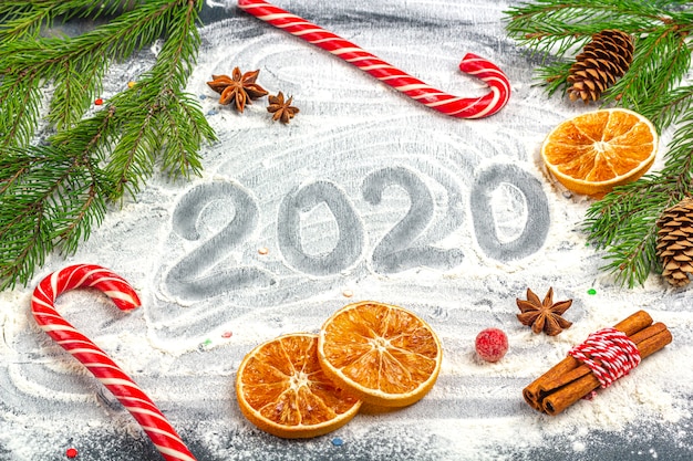 Inschrift des guten Rutsch ins Neue Jahr 2020 und Rahmen von Tannenzweigen, von Kegeln, von Sternanis, von Zimt und von getrockneten Orangen