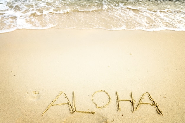 Inscrição Aloha escrita na praia de areia com onda oceânica - espaço livre. efeito de tom de cor vintage