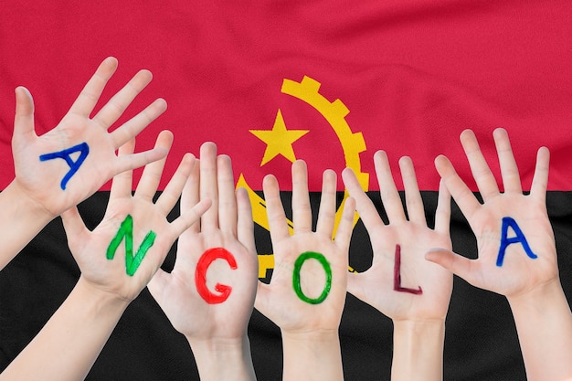 Inscrição angola nas mãos das crianças no contexto de uma bandeira agitando de angola