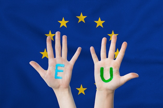 Inscrição da UE nas mãos das crianças contra a superfície de uma bandeira da União Europeia a tremular.