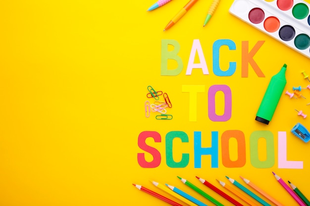 Inscrição de volta à escola com material escolar em fundo amarelo. Letras coloridas