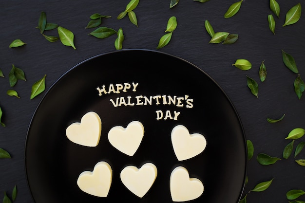 Inscrição em forma de coração de chocolate branco doce feliz dia dos namorados em uma placa preta com folhas verdes