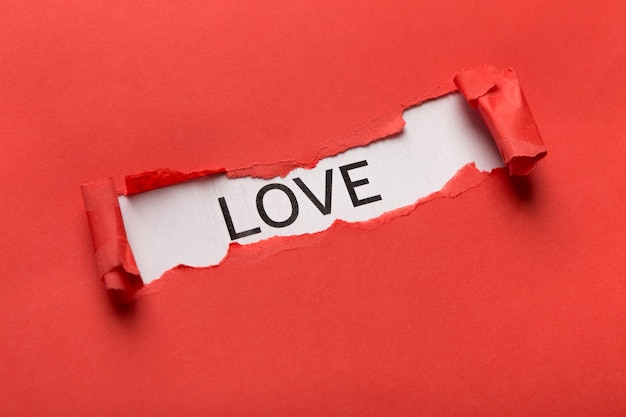 Inscripción de amor detrás de papel rojo rasgado. Concepto de romance, frase para pancarta, póster o diseño de ropa, espacio de copia