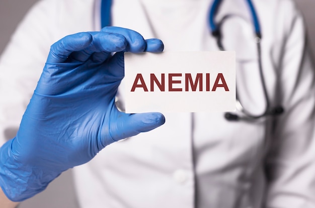 Inscripción de anemia en papel en la mano del médico en guantes azules closeup