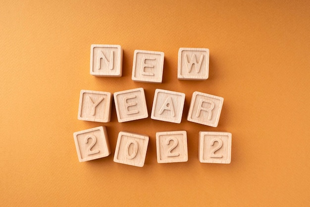 Foto la inscripción año nuevo 2022 en cubos de madera cubos de madera con letras sobre fondo naranja tarjeta de año nuevo