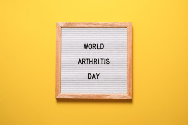La inscripción día mundial de la artritis de un pizarrón blanco sobre un fondo amarillo brillante.