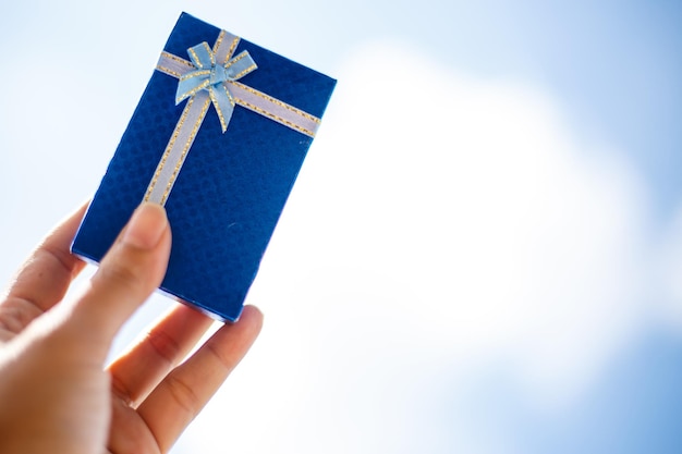 Inscripción del Día del Padre Feliz con mano humana sosteniendo el presente sobre fondo de cielo azul Saludos y regalos