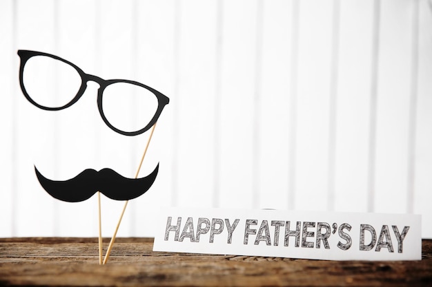 Foto inscripción de feliz día del padre con bigote de papel y gafas en una mesa de madera