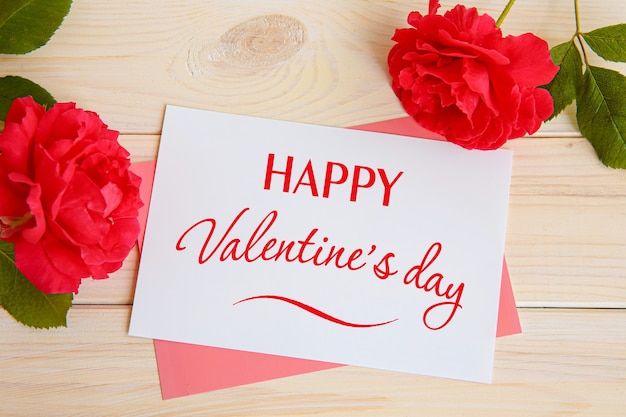 Inscripción feliz día de San Valentín, rosas rojas y una tarjeta