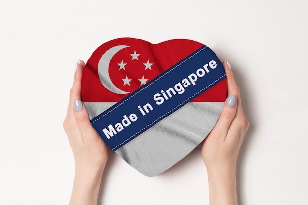 Inscripción hecha en Singapur la bandera de Singapur. Manos femeninas que sostienen una caja en forma de corazón.