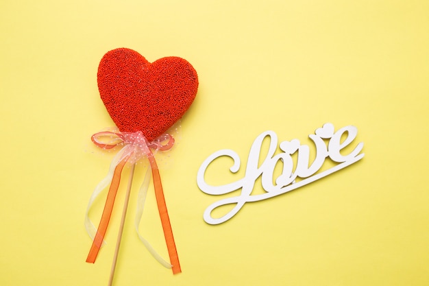 Inscripción de letras de madera amor sobre un fondo amarillo aislado. Corazón en forma de caramelo en un palo.