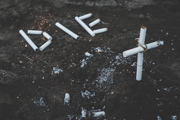 Inscripción muere en el suelo forrado con cigarrillos. tumba de cigarrillos y cigarrillos con humo de tabaco. Concepto anti-tabaco. Los peligros de la nicotina para la salud. fotos en tonos oscuros.