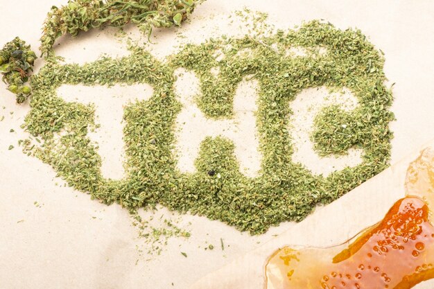 Inscripción de palabra THC con cogollos de cannabis triturados verdes y cera dorada con alto thc.