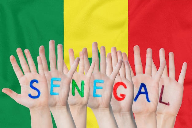 Inscripción Senegal en las manos de los niños contra una bandera ondeante del Senegal