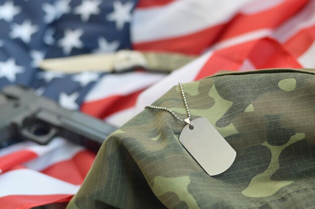 Foto insignia de identificación del ejército con balas de 9 mm y pistola en la bandera doblada de los estados unidos y el uniforme de camuflaje