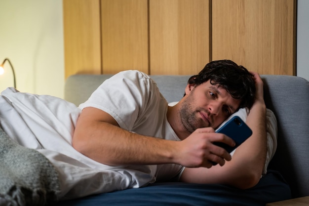 Insomnio y teléfonos móviles Un hombre está acostado en una cama y usa un teléfono inteligente Un hombre joven está acostado en la cama usando un teléfono inteligente