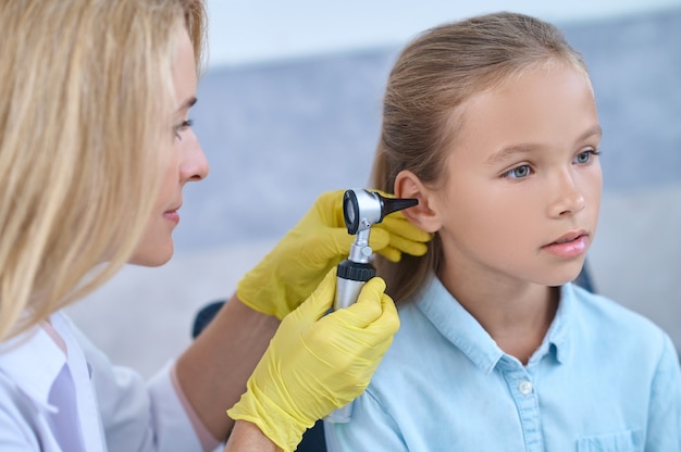 Foto inspeção, otoscópio. otorrinolaringologista concentrada em luvas amarelas com otoscópio perto da orelha de uma linda garotinha de cabelos compridos