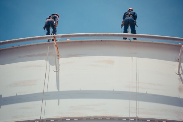 Inspección de acceso por cuerda de dos trabajadores masculinos de la industria del tanque blanco de almacenamiento de espesor