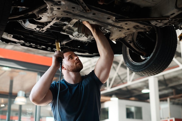 Inspección de antorchas y mecánico con coche en el garaje para mantenimiento de servicio o reparación para la seguridad Ingeniería automotriz ligera y trabajador industrial masculino comprobando la parte inferior del vehículo para detectar fugas de aceite en el taller