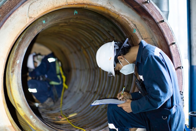 La inspección de dos trabajadores masculinos midió el espesor circular de la tubería del serpentín del espesor mínimo del escaneo de la caldera en un espacio confinado peligroso.