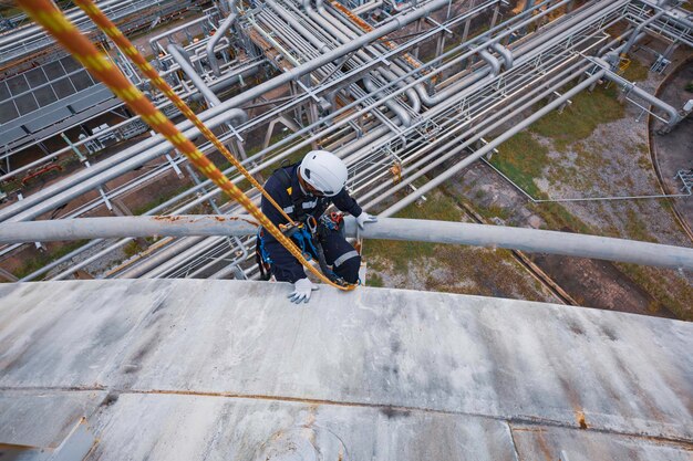 Inspección de trabajadores masculinos que usan la primera línea de seguridad de la cuerda del arnés de seguridad que trabaja en un lugar alto debajo del aislamiento de tuberías largas de acero que fluye y el codo de la tubería