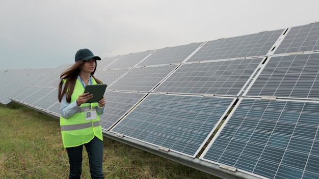 Inspektorin-Ingenieurin geht mit einem digitalen Tablet-PC auf eine Station für erneuerbare Energien und überprüft die Installation von Sonnenkollektoren. Sonnenkollektorfeld. Saubere Energieerzeugung. Grüne Energie.