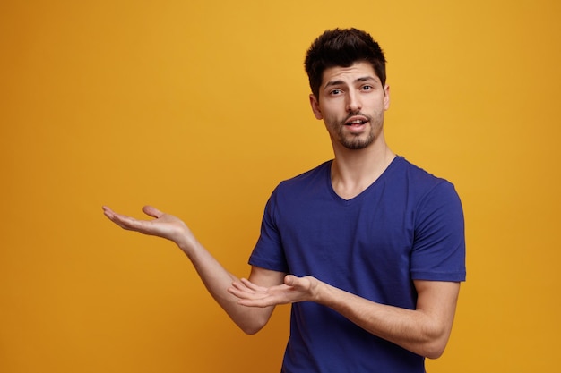 Inspirado jovem bonito olhando para a câmera mostrando as mãos vazias no fundo amarelo