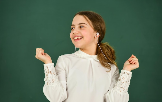 Inspirado con la música. concepto de aprendizaje electrónico. educación en el hogar educación en línea. De vuelta a la escuela. niña pequeña con auriculares en la pizarra. escuchar audiolibro. chica genial con auriculares escuchando música.