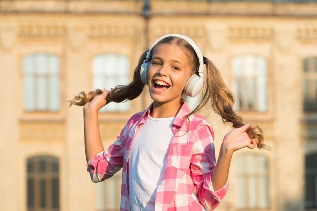 Inspirado en su canción favorita, una niña pequeña escucha música, un niño con auriculares, felicidad infantil, un niño feliz de humor juguetón, tiene cabello rubio, un peinado lindo y elegante, tiempo libre en primavera.