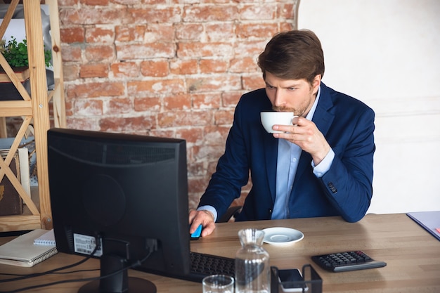 Inspirado tomando café, tareas de lectura. El joven, gerente, vuelve a trabajar en su oficina después de la cuarentena, se siente feliz e inspirado. Volviendo a la vida normal. Negocios, finanzas, concepto de emociones.