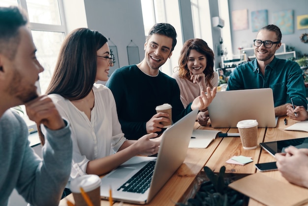 Inspirado para trabajar juntos. Grupo de jóvenes modernos en ropa casual elegante discutiendo algo y sonriendo mientras trabaja en la oficina creativa