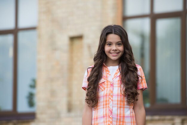 Inspírate a ser bella. Niña feliz con pelo largo ondulado sonrisa urbana al aire libre. Salón de belleza. Look de moda. Estilo casual. Ropa de moda. Niñez y niñez. Día internacional de la niña.