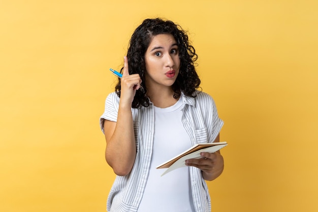 Inspirierte Frau, die in Notizbuch aus Papier schreibt und eine neue ausgezeichnete Idee hat, die den Finger hochhebt