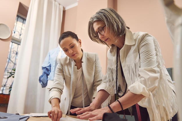 Inspiriertes und kompetentes Team aus zwei unterschiedlichen Modedesignerinnen, die in einem Bekleidungsdesign- und Schneideratelier mit Schnittmustern arbeiten