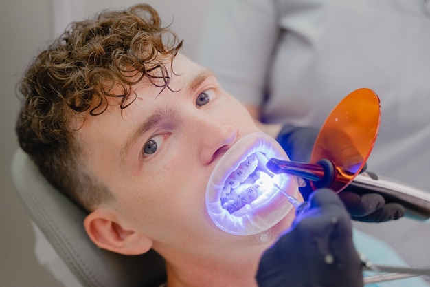 Instalação de aparelhos para um jovem um ortodontista brilha luz ultravioleta sobre os aparelhos